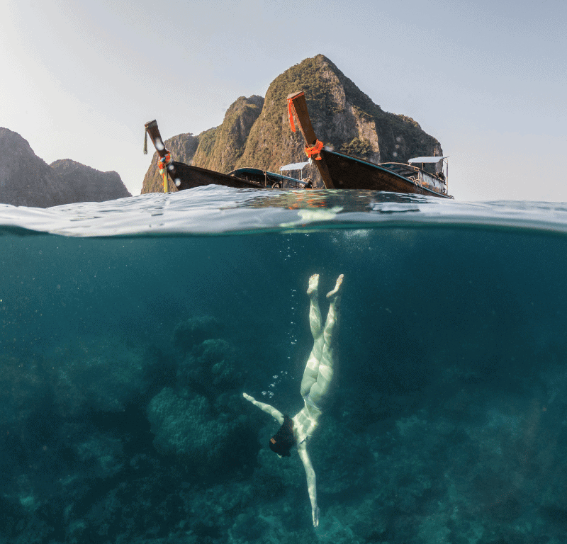 Girl snorkeling with long tail in the background in Phi Phi Island